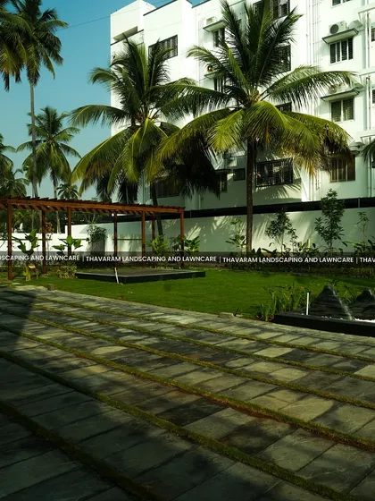A wide view of a large outdoor space, featuring a stone paver patio, a lush lawn, a wooden pergola, and a modern water feature.