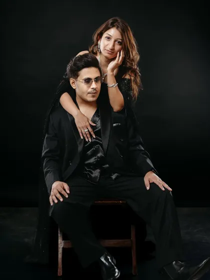 A posed yet intimate studio portrait with a classic feel. The woman leans gently on her seated partner, creating a composition that is both strong and tender. The dramatic lighting on the black backdrop adds a touch of old-world glamour.