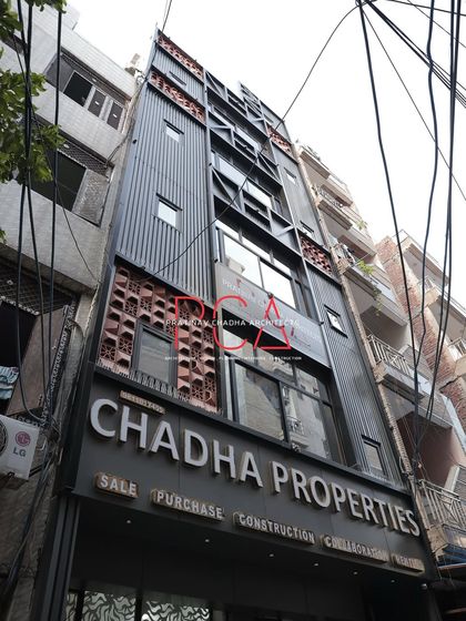 A daytime, low-angle shot of the Chadha Properties office. This view emphasizes the building's height and the industrial-chic aesthetic created by the dark ACP louvers and terracotta accents.