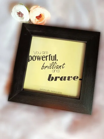 Another view of the "powerful, brilliant and brave" quote frame, styled with small flowers to highlight its aesthetic appeal as desk or wall decor.