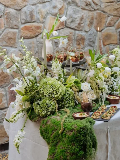 We call this our Earth Table, a signature setup for intimate feasts. A river of fresh moss, white florals, and soft candlelight runs down the center, creating a tablescape that is both grounded and ethereal against our natural stone walls.