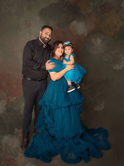 A loving family portrait with the mother and daughter in stunning matching teal gowns. The warm, painterly backdrop adds a classic and artistic touch to the image.
