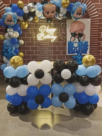 This Boss Baby setup features a unique cake table made of balloons. The backdrop is a brick wall pattern with a neon sign and character posters.