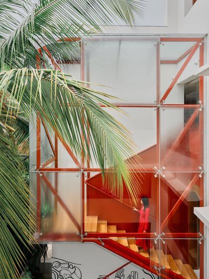 The glass-encased red staircase is framed by palm trees, creating a vibrant tropical image that highlights the home's unique character.