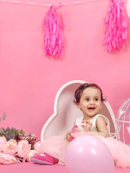 A cheerful first birthday girl in a pink wonderland. This setup features pink balloons, floral arrangements, and birdcages for a whimsical garden party feel.