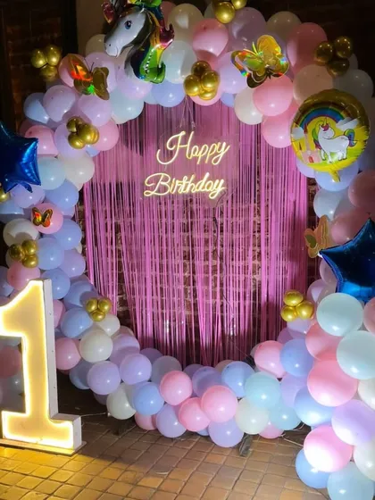A full ring backdrop for a first birthday, decorated with pastel balloons, a unicorn head foil balloon, and a glowing neon sign.