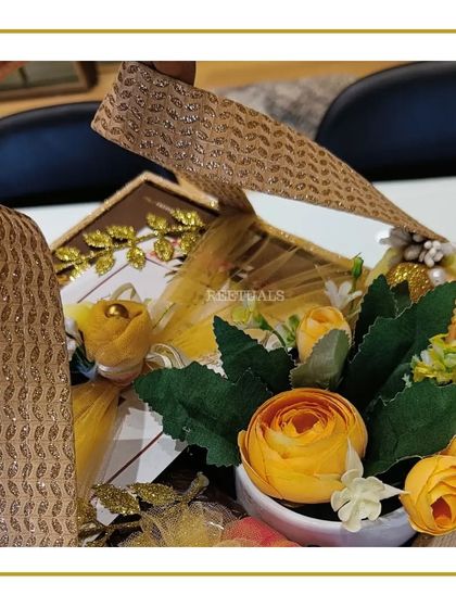 A glimpse inside a golden-themed birthday hamper, showing a floral arrangement in a ceramic pot.