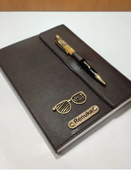 A personalized brown leather diary with a 2023 glasses charm, paired with a gold flake pen.