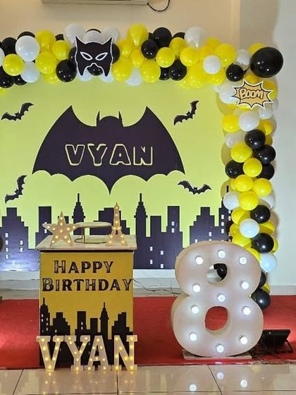 A striking Batman themed birthday setup for an 8th birthday. The iconic Gotham city skyline backdrop, yellow and black balloon arch, and life-size Batman cutouts create a powerful superhero atmosphere.