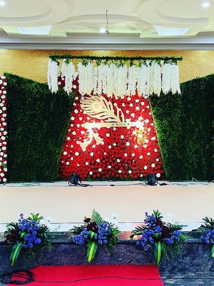 A large-scale stage for a naming ceremony at Manasa Banquet Hall. The design uses panels of red flowers and green foliage, with a central floral motif and a dedicated floral ring for the cradle.