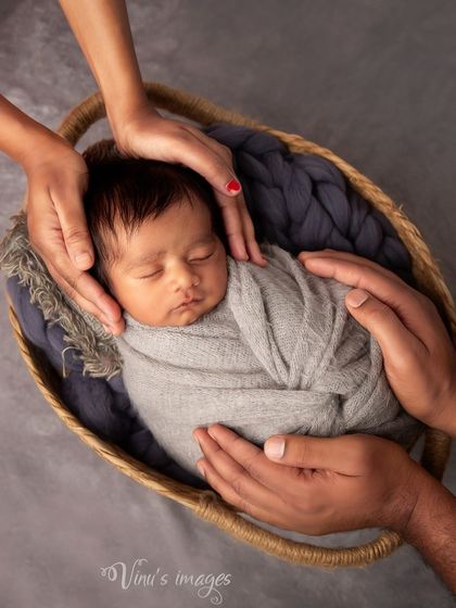 Held in loving hands. This symbolic newborn photo shows the baby sleeping peacefully in a basket, cradled by the hands of both parents, representing their protection and love.