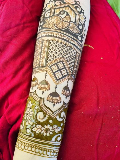 A detailed armband combining several auspicious symbols: a peacock, a swastika, and hanging jhumkis.