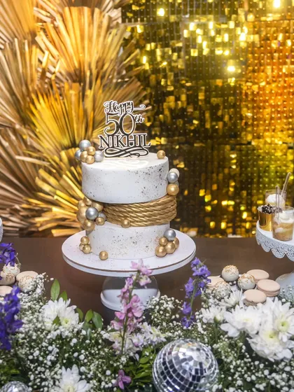 This two-tier cake was designed for a glamorous 50th birthday bash with a "Bling & Bubbly" theme. We used a clean white finish, elegant gold rope detailing, and silver and gold spheres to create a sophisticated and celebratory centerpiece. It was part of a full dessert table that matched the party's chic aesthetic.