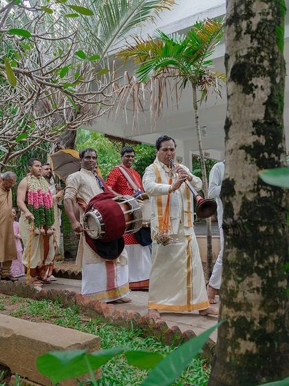 The groom's procession walking along a garden path, accompanied by traditional drummers.
