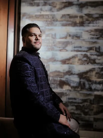 A classic portrait of the groom, seated and looking away thoughtfully. The dark, rich tones of his sherwani add to the elegance of the shot.