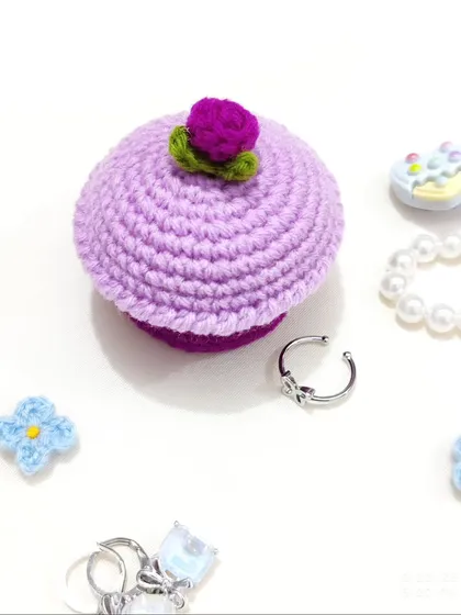 A top-down view of the purple cupcake ring box, surrounded by small rings and accessories.