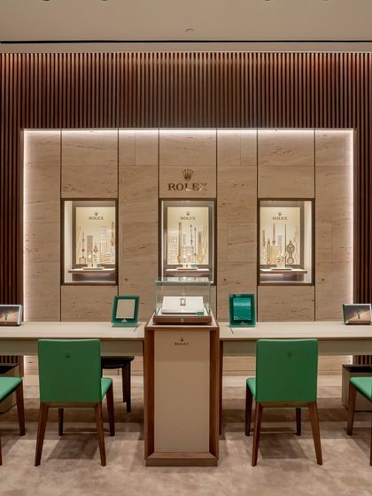 The main consultation area at the Rolex boutique features a clean, symmetrical design that focuses attention on the timepieces. Slatted wood panelling and soft, integrated lighting create a refined atmosphere for patrons to engage with the products.