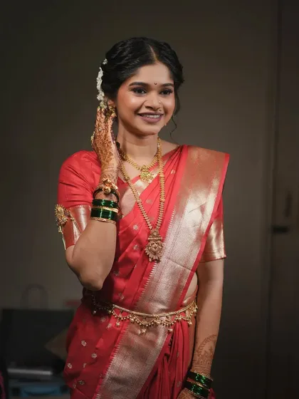 A beautiful portrait of a bride in a red saree. Her makeup is soft and romantic, with a messy bun and delicate jewelry completing the look.