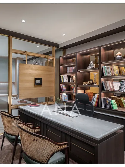 This managing director's cabin was custom-designed to feel luxurious yet minimal. The space features a Michelangelo stone top desk, a book cabinet with a brown mirror back, and glass partitions framed in MS with veneer cladding for a sophisticated corporate interior.