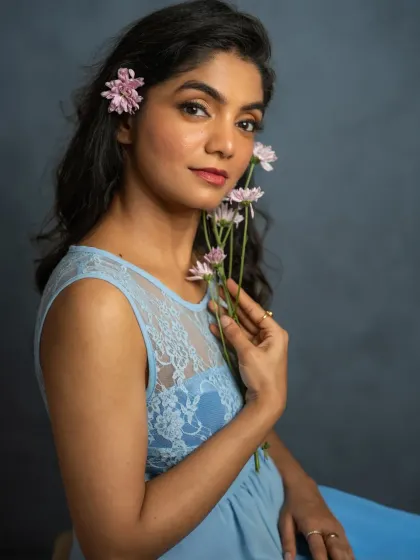 Adding a simple prop like flowers can introduce a touch of softness and narrative to a portrait. Here, the delicate blooms complement Mridula's gentle expression and the soft blue of her dress, creating a portrait that feels both fresh and timeless.