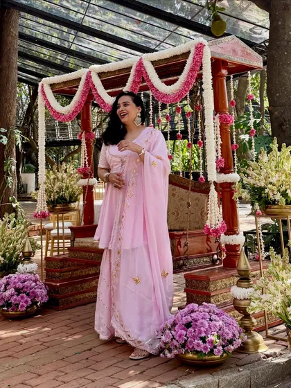 Dressed in a lovely pink sharara set for a baby shower, which has a similar vibe to a daytime wedding function. The floral swing decor adds a beautiful, traditional touch.