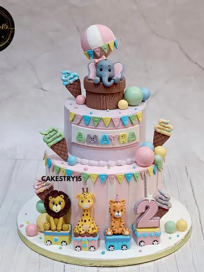A playful two-tier jungle train cake for a second birthday. This choco-vanilla cake features an elephant in a hot air balloon and a train carrying a tiger, giraffe, and lion.