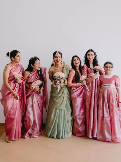 A happy group photo of the bride with her bridesmaids, all holding bouquets and sharing a laugh during the Haldi festivities.