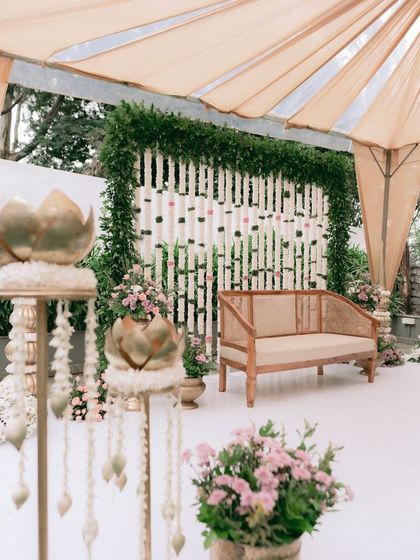 A wider view of the outdoor engagement setup. The simple tent, cane sofa, and floral backdrop create an inviting and elegant space for an intimate celebration.