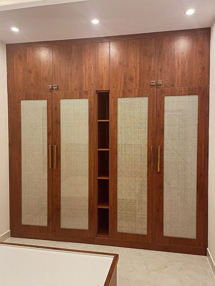 Cane rattan shutters are a popular trend for openable wardrobes. This design combines the natural texture of cane with a rich wood laminate and a central open shelving unit for display.