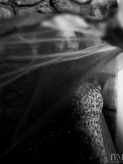 An artistic black and white shot of the bride through her veil. The motion blur and sparkling details on her dress create a dreamy and mysterious bridal portrait.