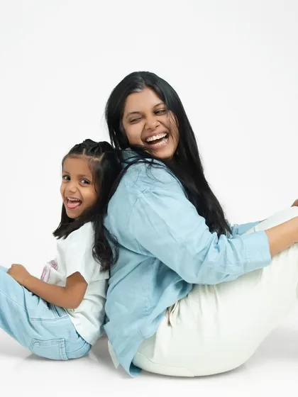 Leaning back-to-back, a mother and daughter share a laugh. This pose is fun and dynamic, showing their close and playful relationship.