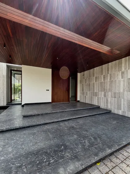 The entryway at Rosewood Farmhouse is raised on broad steps, with an oversized covered porch that balances the facade. Warm wood details soften the grey stone, creating a welcoming contrast that sets a grand yet grounded tone.