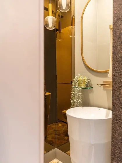 A peek into a glamorous powder room. The gold-tinted mirror reflects the warm glow of the pendant lights, creating a moody and sophisticated atmosphere.