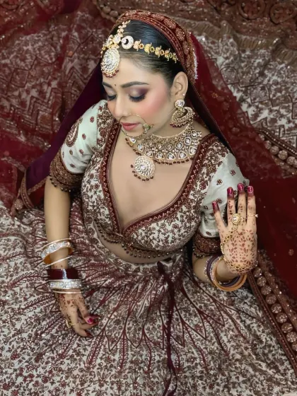 An aerial view of the bride seated, showcasing the full expanse of her intricately embroidered lehenga. Her pose highlights the detailed henna and makeup.