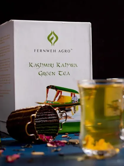 A styled product shot of Fernweh Agro's Kashmiri Kahwa Green Tea. The composition includes the packaging, tea bags, and loose tea leaves with rose petals to give a complete product story.