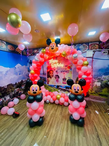 A Mickey Mouse themed birthday party in a restaurant, using a pink, red, and black color scheme for the balloon arch.
