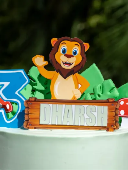 A close-up of the friendly lion topper and custom name plaque on this jungle themed cake.