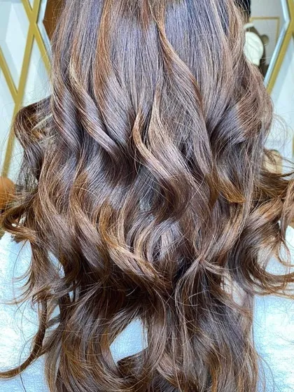 This image showcases a beautiful balayage with light brown and caramel tones. The hair is styled in defined curls to emphasize the dimension and texture of the color.