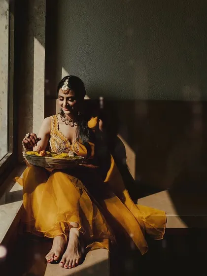 A stunning, artistic shot of the bride sitting by a window, the natural light highlighting her yellow outfit and the sunny decor theme.