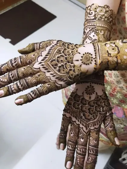 A beautiful pose showing the intricate details of this guest mehendi. The design features a central floral mandala and detailed patterns on the fingers and wrist.