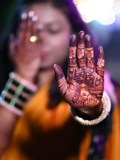 A beautiful out-of-focus shot with the bride's mehndi-adorned hand in the foreground. It highlights the artistry and the rich color of the henna.