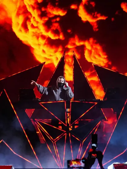 Alan Walker at the decks, with a fiery, explosive visual on the LED screen behind him creating an intense atmosphere.