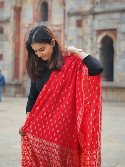 The vibrant red dupatta becomes the centerpiece of this portrait. Her candid, downward glance creates a natural and soft moment, perfect for showcasing traditional wear.