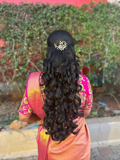 This beautiful half-updo is perfect for a reception. The hair is styled in long, flowing curls and adorned with a delicate pearl accessory for a touch of sparkle.