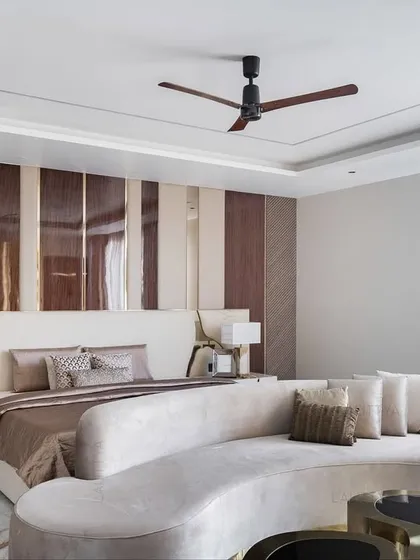 This angle shows the relationship between the bed and the lounge area within the master suite. A custom curved sofa sits at the foot of the bed, which features a striking wall of vertical wood and mirrored panels.