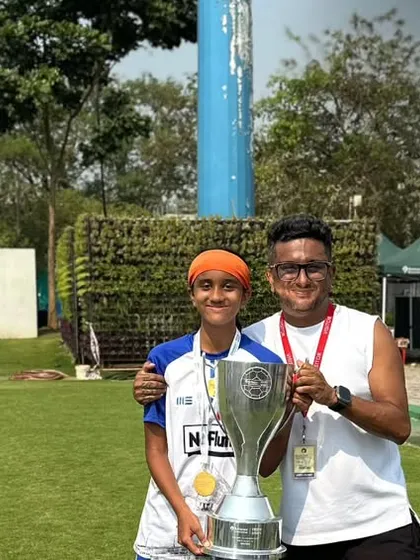 A player and coach celebrating with the championship trophy from the Reliance Foundation Young Champs Football Cup. This highlights the strong bond between our coaching staff and players.