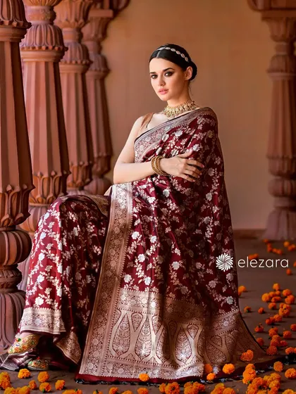 A full seated portrait from the Elezara campaign. The saree is draped elegantly, and the scattering of orange flowers on the floor adds a pop of color and a touch of tradition.