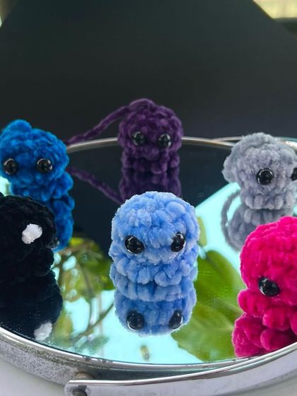 A group shot of my mini octopus keychains in various colors like black, blue, purple, and pink. These are made with a velvety yarn that makes them incredibly soft to the touch.