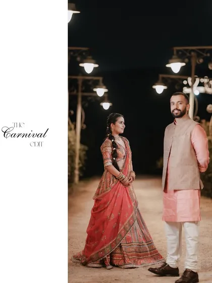 A full-length portrait from "The Carnival Edit". The couple stands under a row of festive lights, perfectly capturing the unique and fun theme of their wedding celebration.