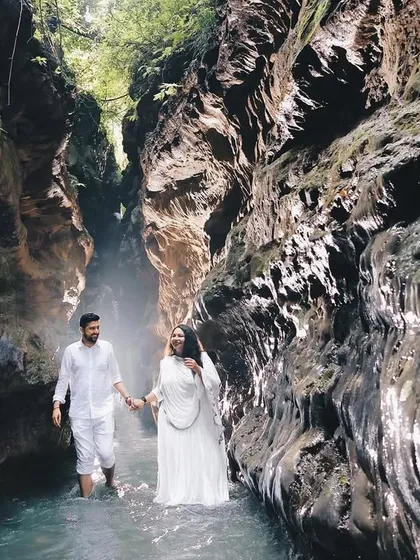 The couple walks hand-in-hand through the water in a narrow canyon, creating a sense of adventure and romance.